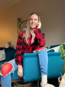 Hypnotherapy Graduate Kryss Huang sitting on her blue couch looking to connect with the SWIHA community.